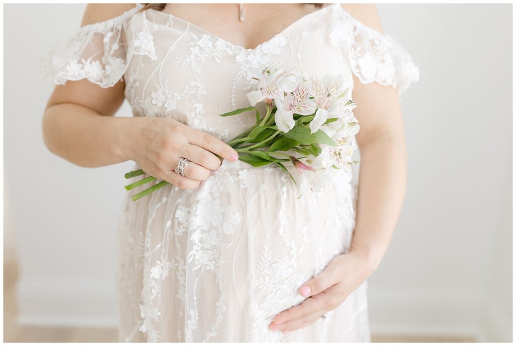 Pregnant mother wearing beautigul white embroidered dress holding flowers and belly.